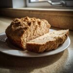 A loaf of homemade soda bread, partially sliced, resting on a white plate in natural light.