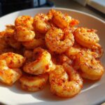 A close-up of plump, cooked air fryer frozen shrimp seasoned with paprika and spices piled on a white plate.