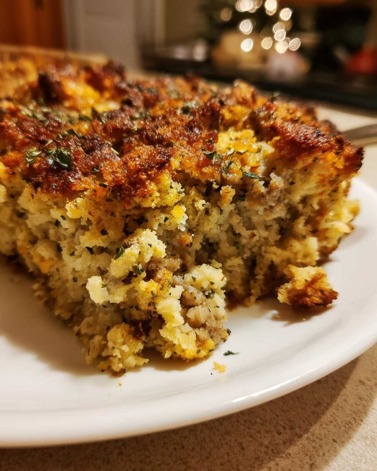 Close-up of a square serving of baked stuffing on a white plate, showing a crispy top and moist interior.