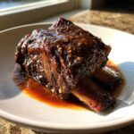 Close-up of tender braised short ribs coated in a thick, glossy brown sauce on a white plate.