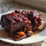 Close-up of tender braised short ribs covered in a rich, dark glaze served on a white plate.