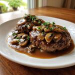 Two perfectly cooked Salisbury steak patties smothered in rich mushroom gravy and garnished with fresh thyme.