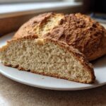 A round loaf of golden brown soda bread with a slice cut open showing the soft interior texture.