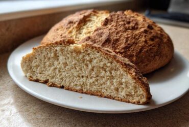 A round loaf of golden brown soda bread with a slice cut open showing the soft interior texture.