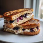 Two halves of golden brown stuffed french toast stacked, revealing a creamy ricotta filling mixed with whole blueberries.