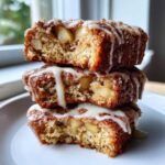 Three stacked pieces of moist baked apple fritters, showing chunks of apple inside and drizzled with white vanilla glaze.