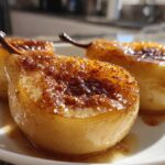 Three glistening baked pears halves topped with caramelized sugar and cinnamon, served on a white plate.