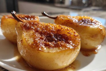 Three glistening baked pears halves topped with caramelized sugar and cinnamon, served on a white plate.