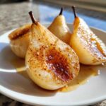 Four halves of glistening baked pears seasoned with cinnamon and syrup served on a white plate.