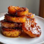 Close-up of stacked, thick-cut candied sweet potatoes slices glistening with a dark, rich glaze.