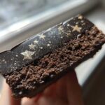A close-up cross-section view of a rich, dark chocolate Capricorn cake slice featuring a black, glossy topping dusted with gold stars.