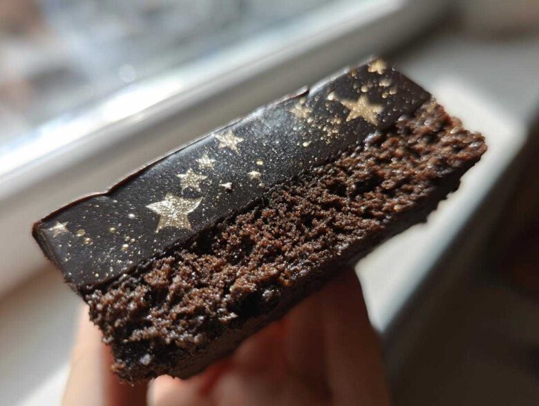 A close-up cross-section view of a rich, dark chocolate Capricorn cake slice featuring a black, glossy topping dusted with gold stars.