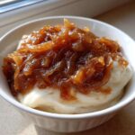 Close-up of a white bowl filled with creamy dip topped generously with dark, glossy caramelized onion dip.