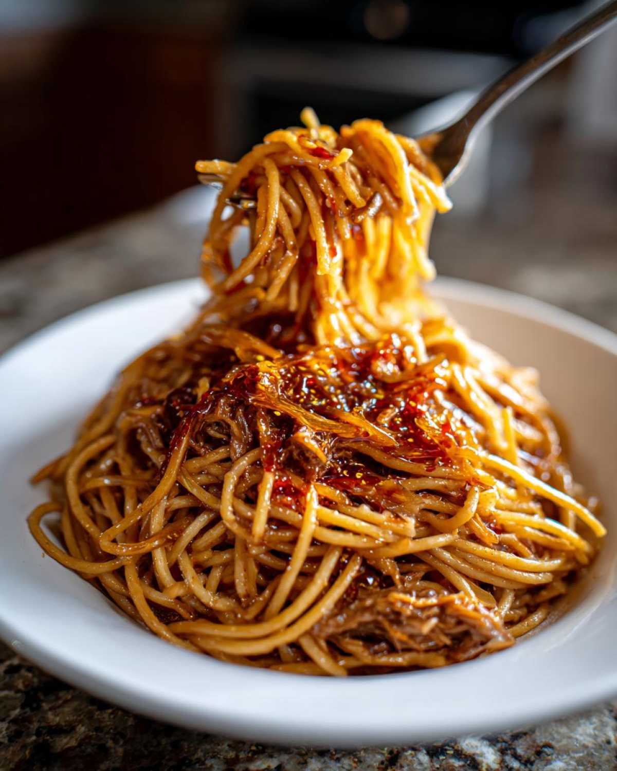 A fork lifting a generous portion of rich, brown caramelized onion pasta from a white bowl.