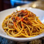 Close-up of a serving of caramelized onion pasta, featuring spaghetti coated in a rich sauce and topped with dark onions.