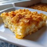 A close-up slice of creamy, cheesy potato casserole topped with golden, crunchy cornflakes.