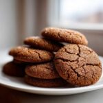 A close-up stack of chewy gingersnap cookies, richly dark brown and coated in sparkling sugar crystals.