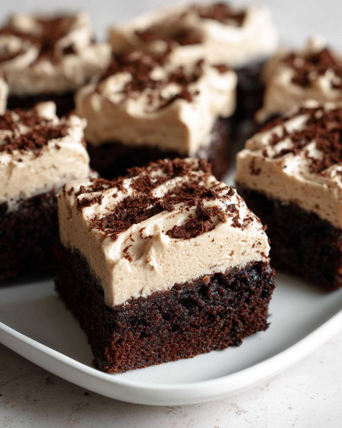 Close-up of a square slice of dark chocolate banana bread brownies topped with light brown frosting and chocolate shavings.