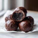 A stack of rich, chocolate-coated Oreo balls, with one cut in half showing the dark, dense interior.