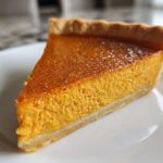 A close-up shot of a perfectly baked slice of classic pumpkin pie on a white plate.