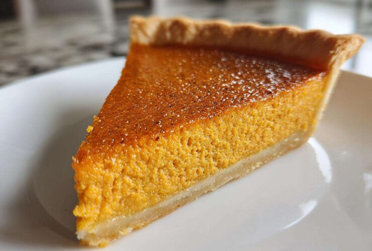 A close-up shot of a perfectly baked slice of classic pumpkin pie on a white plate.