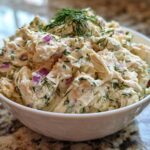 Close-up of creamy cottage cheese chicken salad mixed with red onion and dill, served in a white bowl.