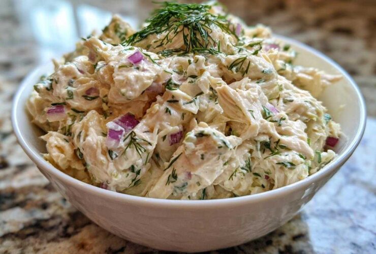 Close-up of creamy cottage cheese chicken salad mixed with red onion and dill, served in a white bowl.