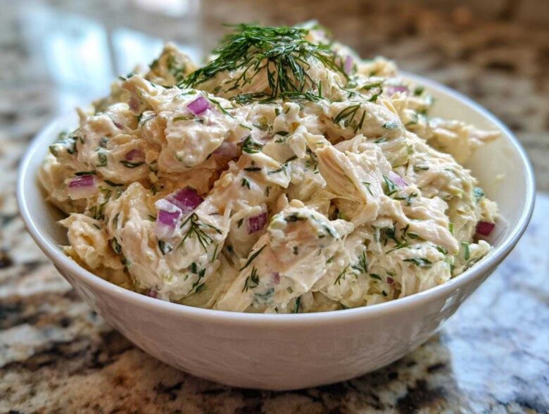 Close-up of creamy cottage cheese chicken salad mixed with red onion and dill, served in a white bowl.