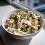 A close-up of creamy cottage cheese chicken salad mixed with red onion and fresh dill, served in a white bowl.