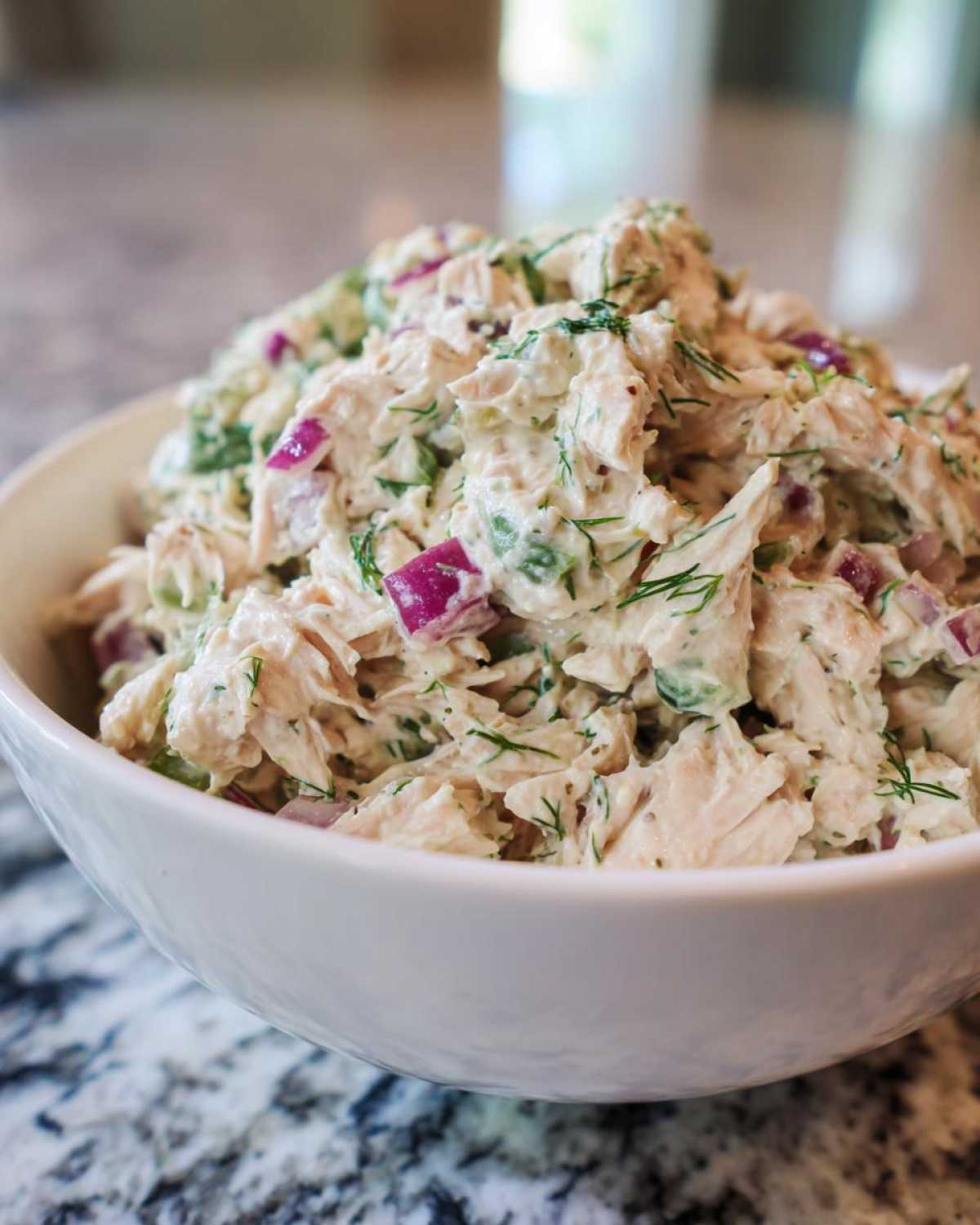 Close-up of creamy cottage cheese chicken salad mixed with red onion and fresh dill, served in a white bowl.