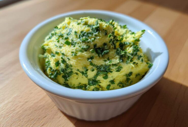 A close-up of bright yellow cowboy butter dipping sauce topped generously with chopped green herbs in a small white bowl.