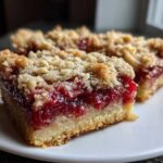 Close-up of two delicious cranberry crumble bars showing the thick, bright red cranberry filling and crumbly topping.