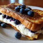 A thick slice of golden brown stuffed french toast filled with creamy white filling and fresh blueberries.