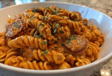Close-up of creamy Cajun sausage pasta featuring rotini noodles and sliced sausage, garnished with parsley.
