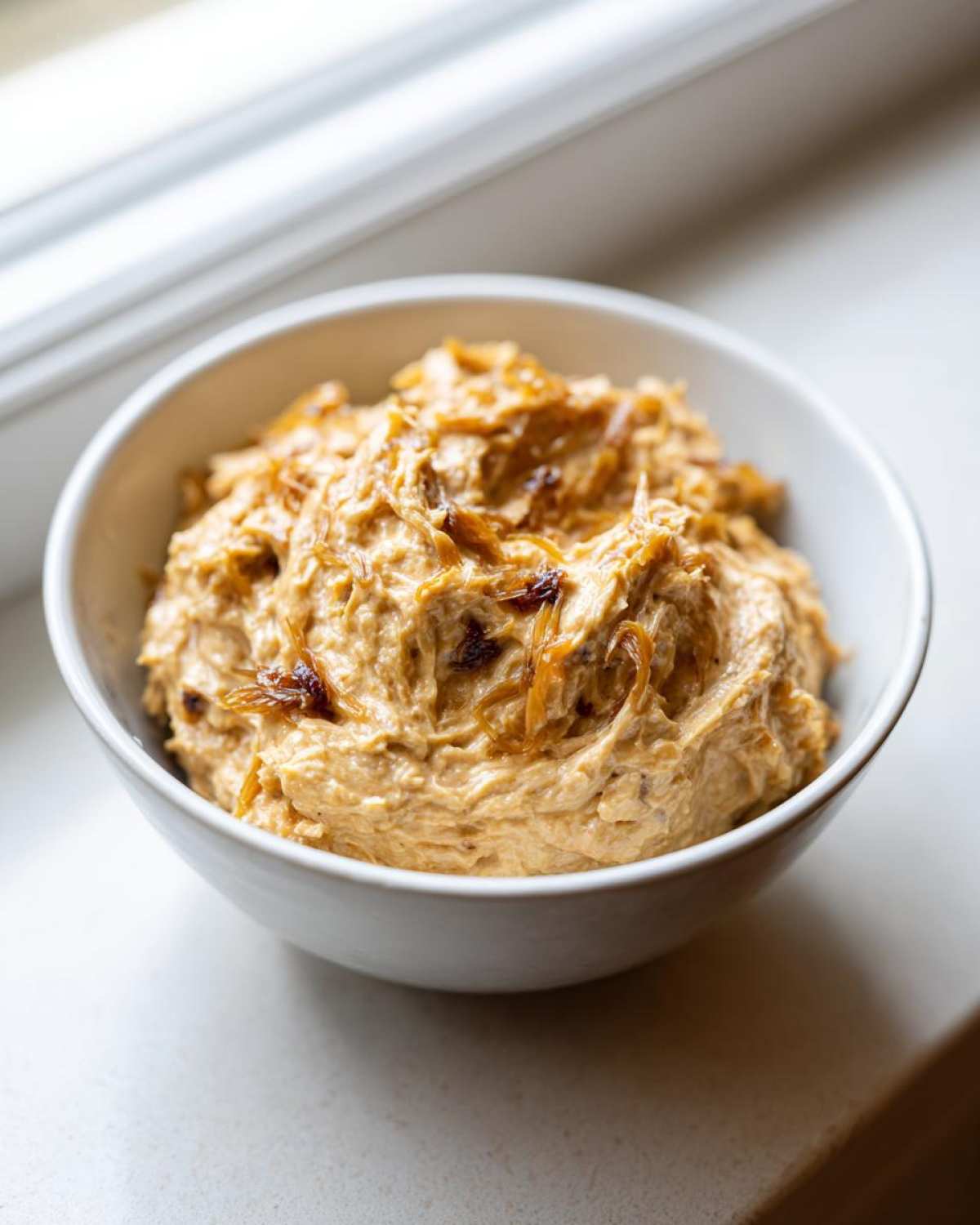 A close-up of creamy caramelized onion dip topped with extra caramelized onions in a white bowl.