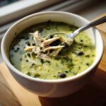 A spoonful of creamy green chicken poblano soup recipe topped with shredded chicken and black beans.