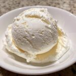 A close-up view of two scoops of white, creamy cottage cheese ice cream served in a small white bowl.