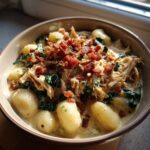 A close-up of creamy crack chicken gnocchi served in a bowl, topped generously with shredded chicken and crispy bacon bits.