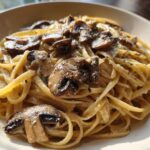 Close-up of creamy mushroom pasta featuring fettuccine noodles coated in a rich sauce and topped with sautéed mushrooms.