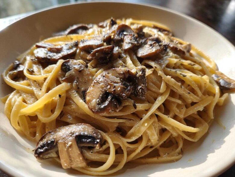 Close-up of creamy mushroom pasta featuring fettuccine noodles coated in a rich sauce and topped with sautéed mushrooms.