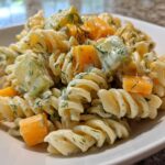 Close-up of creamy pickle pasta salad featuring rotini pasta, dill, pickles, and chunks of cheddar cheese.