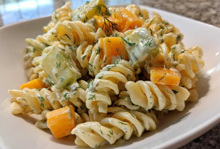 Close-up of creamy pickle pasta salad featuring rotini pasta, dill, pickles, and chunks of cheddar cheese.