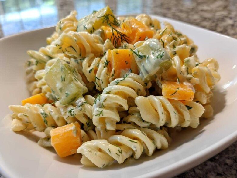 Close-up of creamy pickle pasta salad featuring rotini pasta, dill, pickles, and chunks of cheddar cheese.