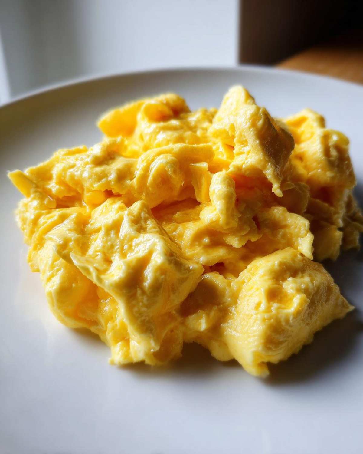 A close-up shot of fluffy, creamy scrambled eggs piled on a white plate.