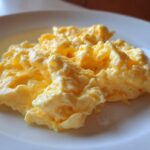 Close-up of fluffy, creamy scrambled eggs served simply on a white plate.