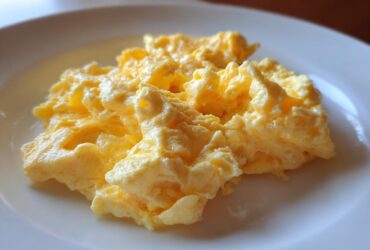 Close-up of fluffy, creamy scrambled eggs served simply on a white plate.