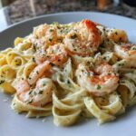 Close-up of creamy shrimp alfredo featuring plump shrimp over fettuccine pasta, topped with Parmesan and parsley.