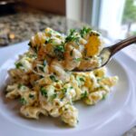 A spoonful of creamy deviled egg pasta salad, garnished with fresh parsley, being lifted from a white plate.