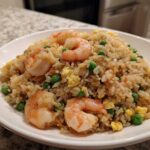 A close-up of a generous serving of shrimp fried rice with visible shrimp, peas, and scrambled egg.