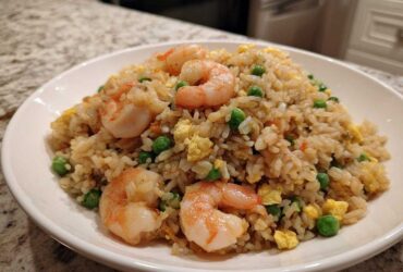 A close-up of a generous serving of shrimp fried rice with visible shrimp, peas, and scrambled egg.